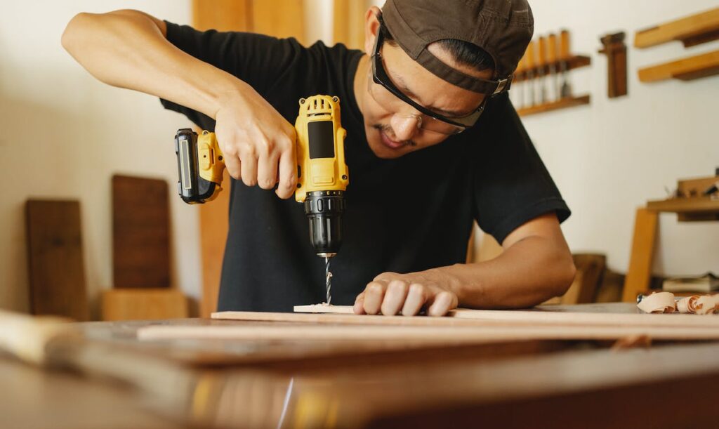 A man works on a piece of wood with a drill