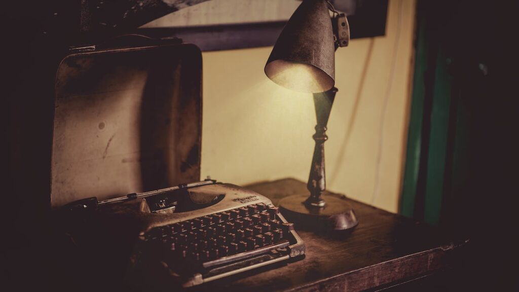 An old desk lamp and gray typewriting on a wooden table.