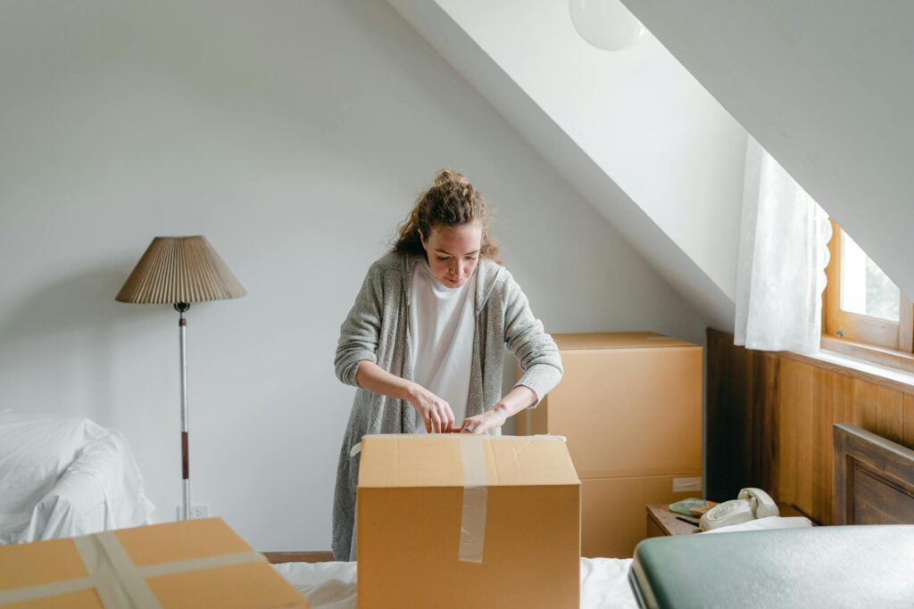 A woman seals a cardboard box in her bedroom